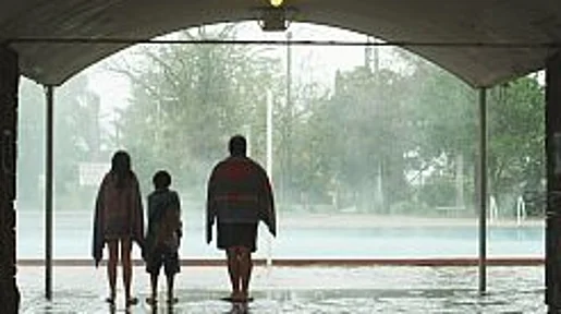 Szenenbild: Die Familie von hinten gesehen, sie schauen auf den im Regen liegenden Swimming-Pool