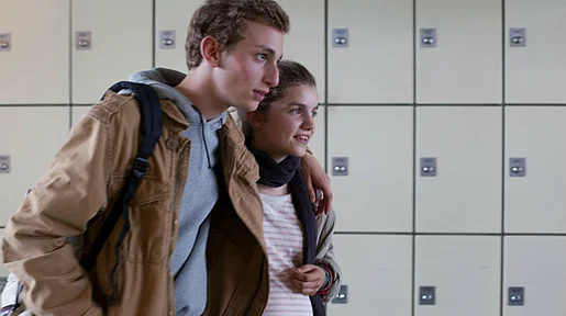 Szenenbild: Maxime und Mélanie Arm in Arm vor einer Wand mit Schließfächern