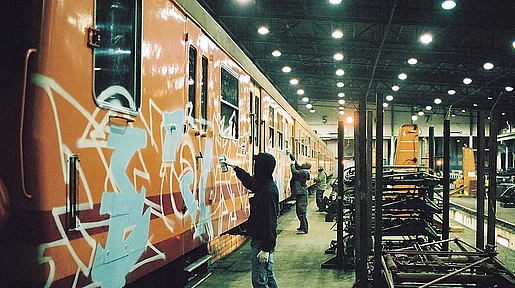 Drei Grafitti-Sprayer besprühen mehrere organgefarbenen Wagons