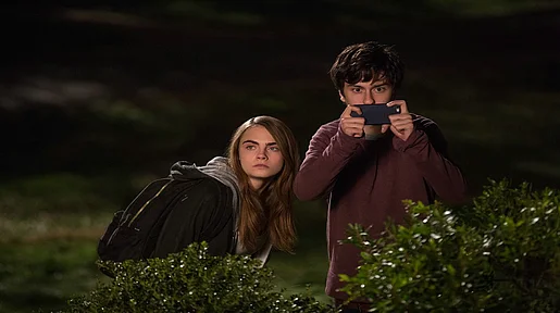 Szenenbild: Margo und Quentin beobachten etwas, halb hinter einer Hecke verborgen in der Nacht