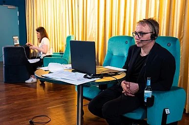 Zwei Personen hinter Laptops vor einem goldgelben Kinovorhang