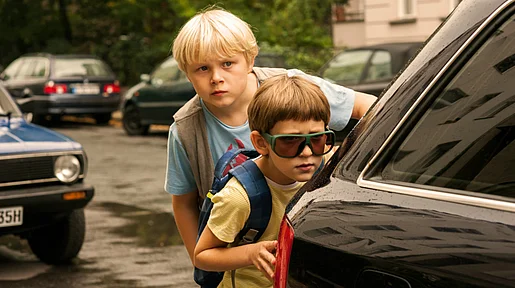 Szenenbild: Rico und Oskar verstecken sich hinter einem Auto, um Beobachtungen anzustellen