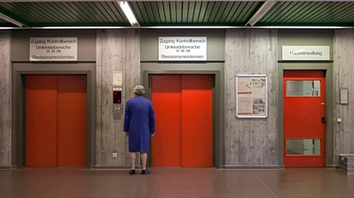 Szenenbild: Ein Mann steht vor drei roten Fahrstühlen