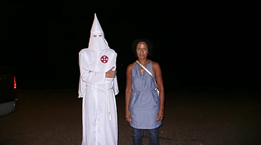 Die Regisseurin Mo Asumang steht neben einer Person in Ku Klux Klan Kleidung