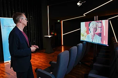 Leopold Gr&uuml;n betrachtet einen Bildschirm, auf dem Staatsministerin Monika Gr&uuml;tters gerade ihr Gru&szlig;wort spricht