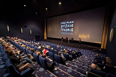 Kinosituation: ein gef&uuml;llter Kinosaal mit G&auml;sten vor der Leinwand