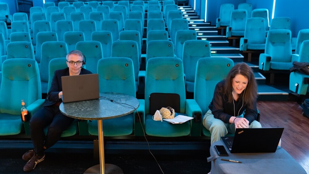 Leopold Grün und Lisa Haußmann mit Computern in einem Kinosaal mit türkisfarbenen Sesseln