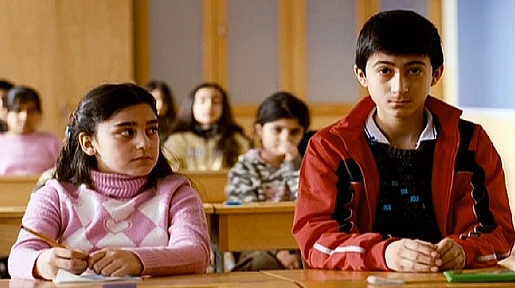 Szenenbild: Zwei Kinder im Klassenzimmer am Tisch sitzend