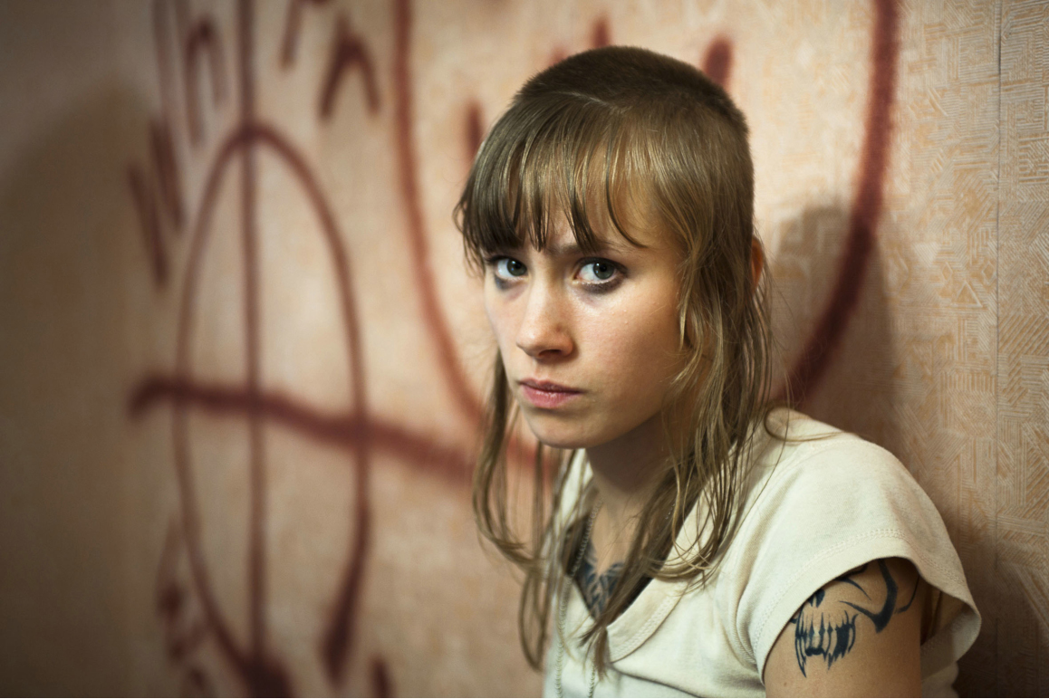 Eine junge Frau steht vor einer Wand mit Graffiti und schaut wütend in die Kamera