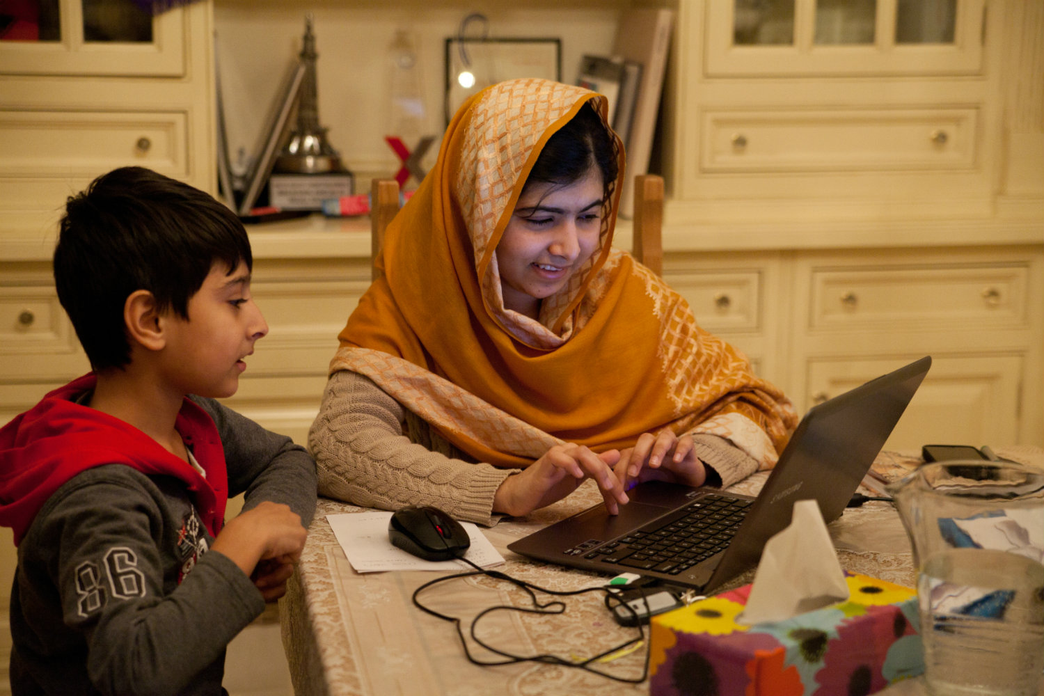 Szenenbild: Malala mit ihrem kleinen Bruder am Küchentisch am Laptop